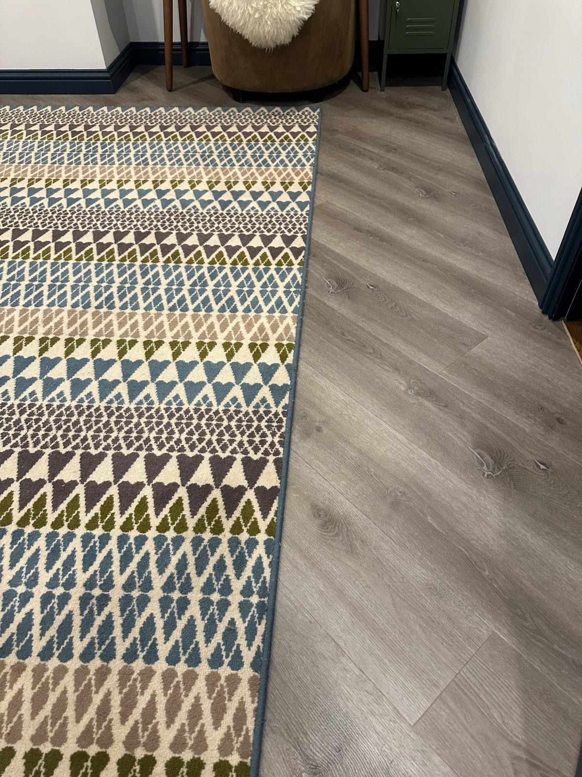 Close detail of the bedroom rug edge and wood-effect LVT flooring in Godalming